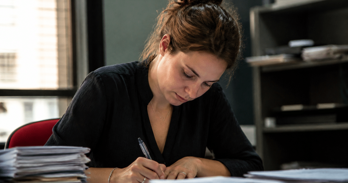 Personne remplissant formulaire administratif à bureau avec documents empiles