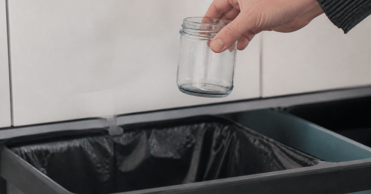 Main tenant pot verre confiture au dessus bac recyclage